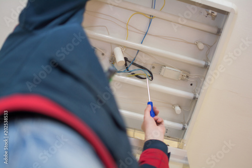 Electrician man worker in uniform installing ceiling fluorescent lamp photo