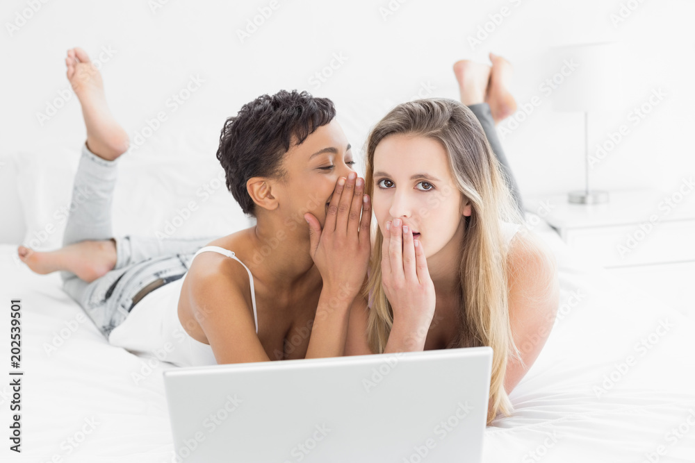Relaxed female friends with laptop gossiping in bed Relaxed female friends with laptop gossiping in bed