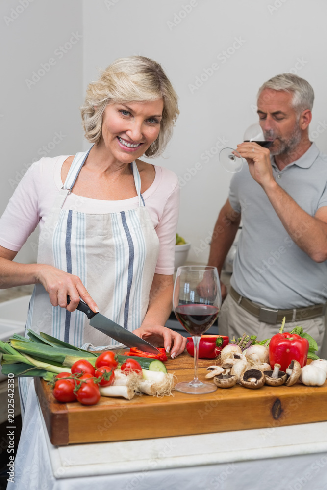 Mature man with wine glass and woman chopping vegetables in kitchen Mature man with wine glass and woman chopping vegetables in kitchen
