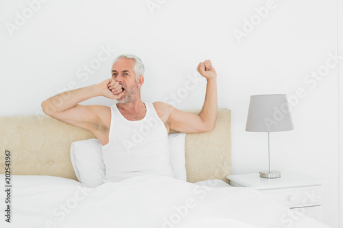 Mature man stretching his arms in bed