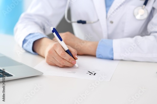 Female doctor filling up prescription form while sitting at the desk in hospital closeup. Physician finishing up examining his patient in hospital and ready to give an advice to help. Healthcar