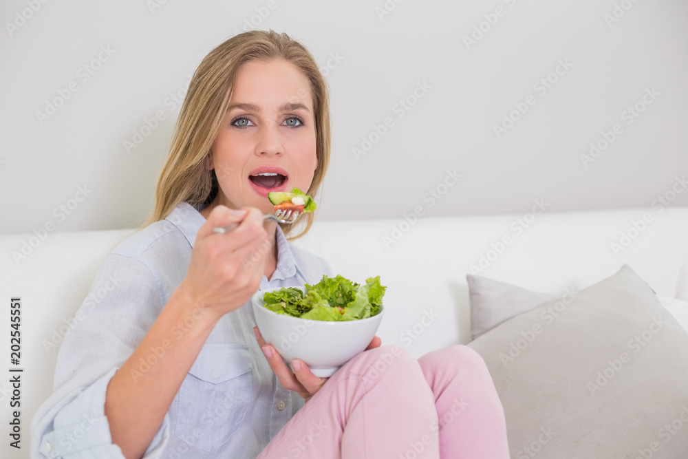 Surprised casual blonde sitting on couch eating salad Surprised casual blonde sitting on couch eating salad