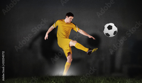 Composite image of football player in yellow kicking against black wall