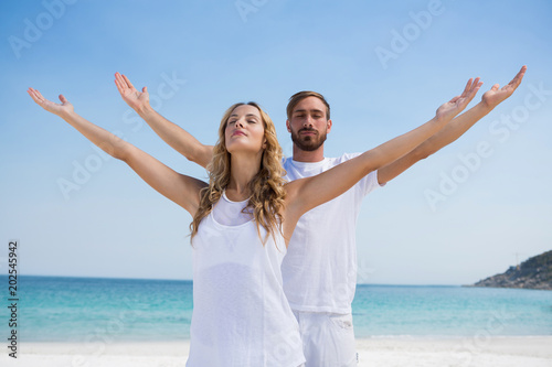 Couple with arms outstretched exercising at beach