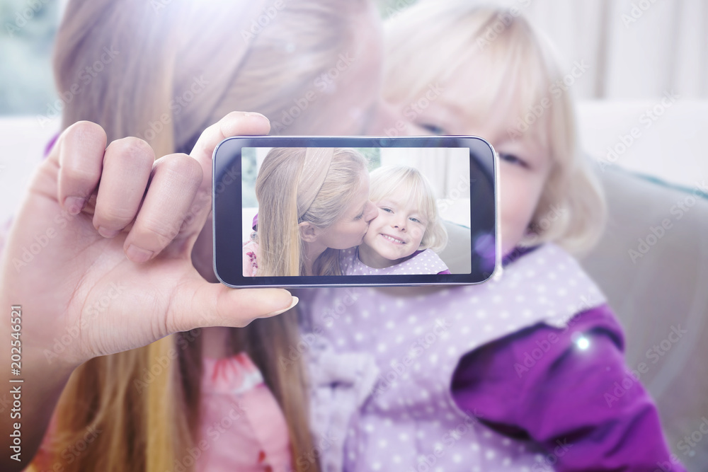Hand holding smartphone showing against happy mother and daughter on the couch