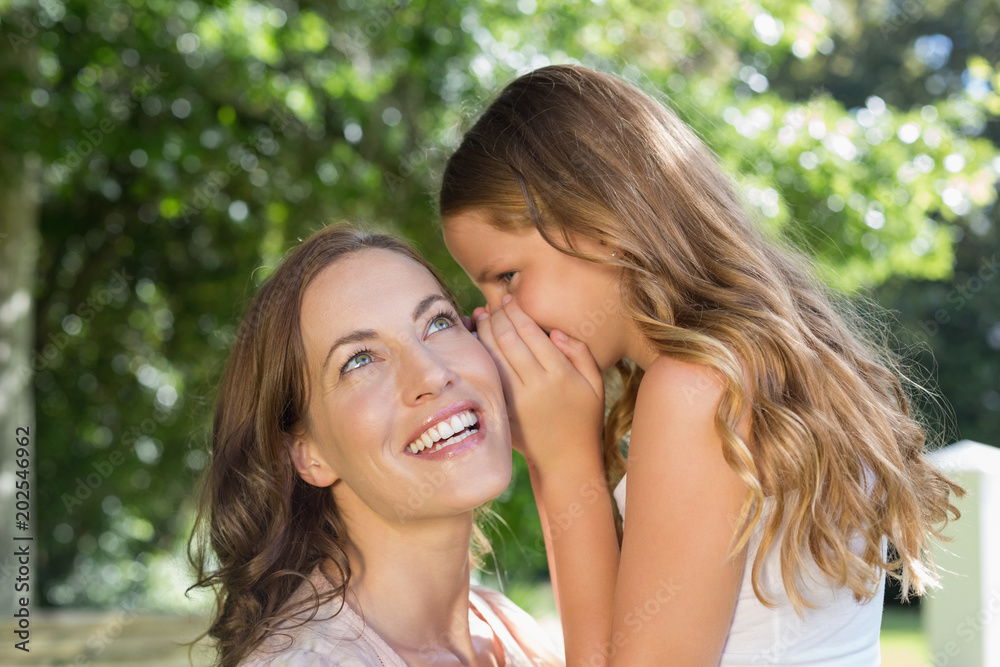Girl whispering secret into mothers ear at park Girl whispering secret into mothers ear at park