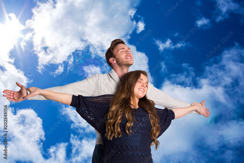 Romantic young couple with arms out against bright blue sky with clouds Romantic young couple with arms out against bright blue sky with clouds