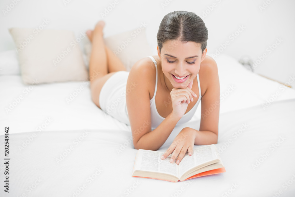 Calm young brown haired model in white pajamas reading a book Calm young brown haired model in white pajamas reading a book