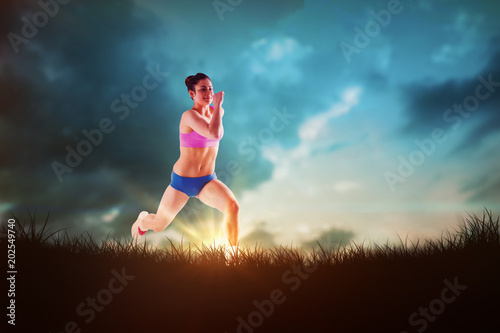 Fit brunette running and jumping against blue sky over grass