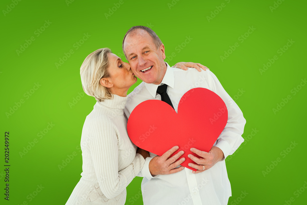 Older affectionate couple holding red heart shape against green vignette