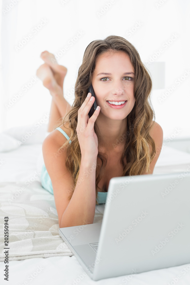 Relaxed woman using mobile phone and laptop in bed Relaxed woman using mobile phone and laptop in bed