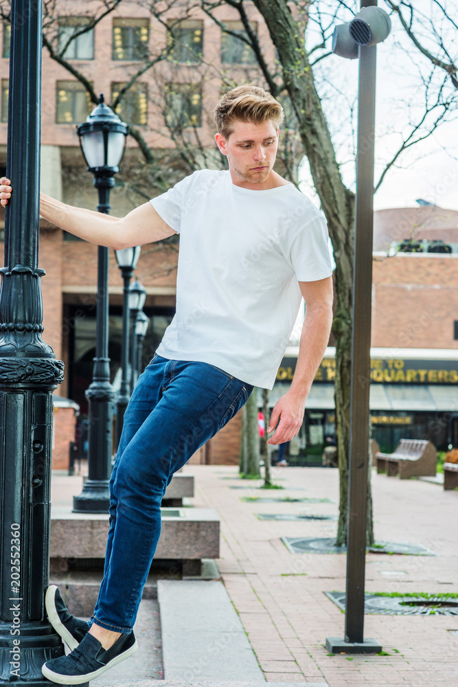 Young Man Summer Street Casual Fashion in New York, wearing white T shirt, blue  jeans, black casual shoes, standing on black light pole, looking down..  foto de Stock | Adobe Stock