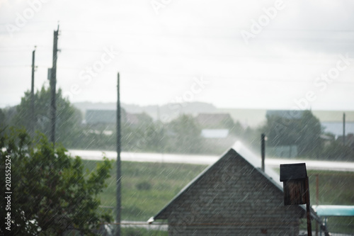 Defocused rainy image from country house, tree, pillars and highway. Focusing on rain. Rainy weather outside city.