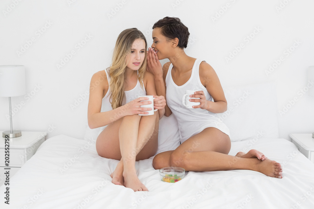 Relaxed female friends with coffee cups gossiping in bed Relaxed female friends with coffee cups gossiping in bed