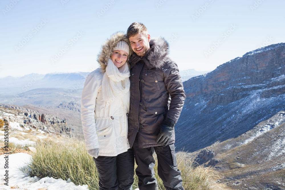 Smiling couple in fur hood jackets against mountain range