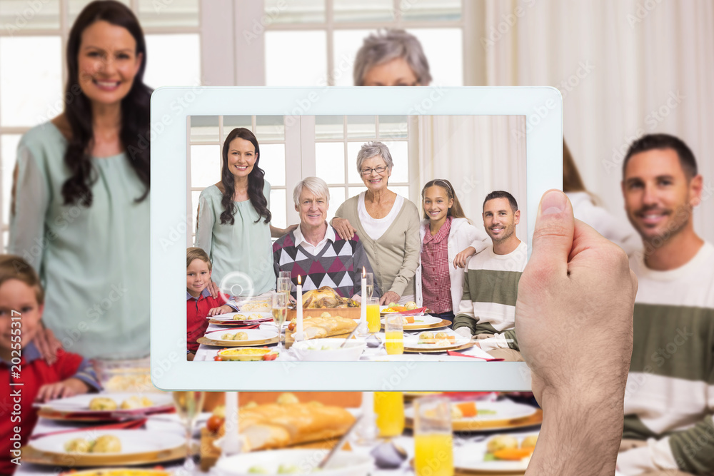 Hand holding tablet pc against happy extended family at christmas dinner posing at camera