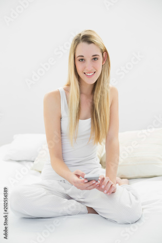 Beautiful calm woman holding her smartphone sitting on her bed © WavebreakmediaMicro