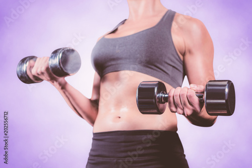 Muscular woman lifting heavy dumbbells against purple background