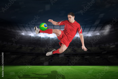 Fit football player jumping and kicking against large football stadium with fans in yellow © vectorfusionart