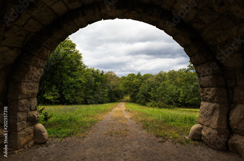 Old stone archway with dirt road leading into distant trees