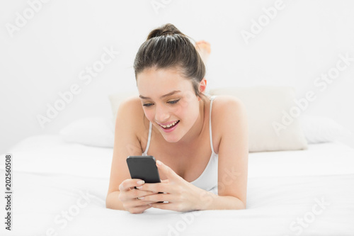 Happy casual woman looking at mobile phone in bed