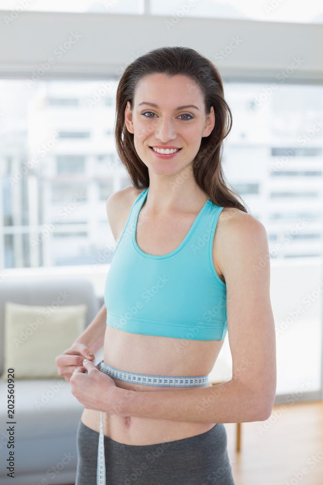 Toned woman in sportswear measuring waist in fitness studio