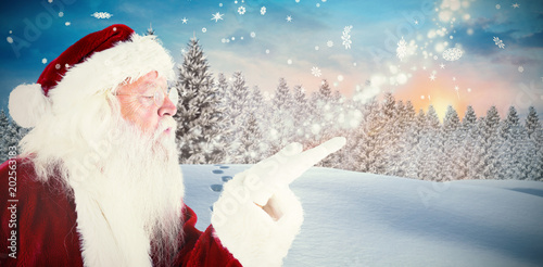 Santa claus blowing against fir tree forest in snowy landscape