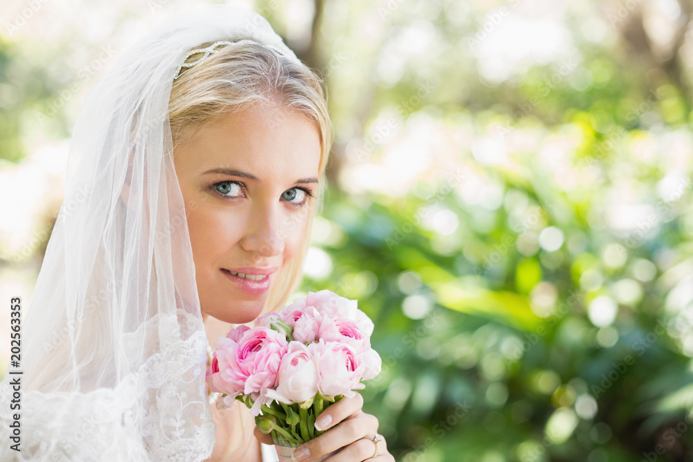 Smiling bride wearing veil holding bouquet looking at camera Smiling bride wearing veil holding bouquet looking at camera