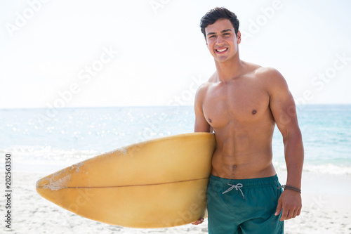 Portrait of shirtless muscular man holding surfboard at beach