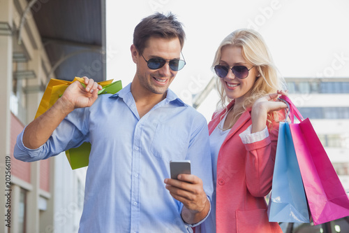 Stylish young couple looking at smartphone holding shopping bags