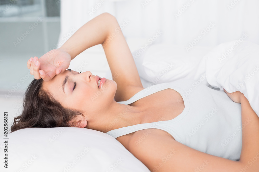 Sleepy young woman suffering from headache with eyes closed in bed Sleepy young woman suffering from headache with eyes closed in bed