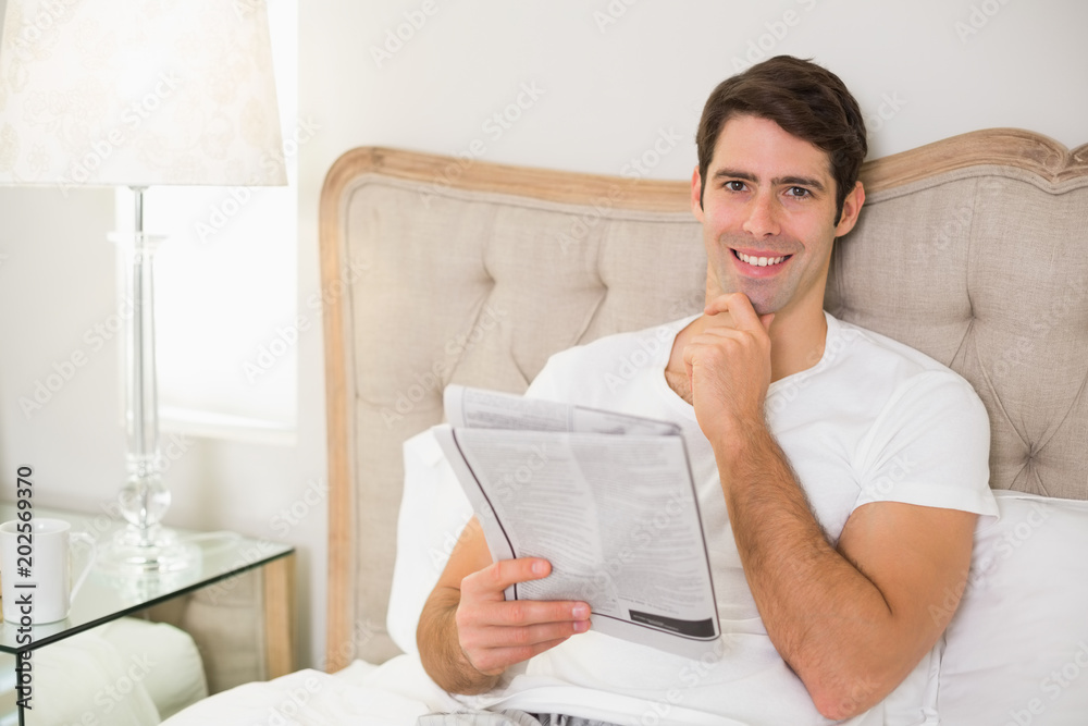 Smiling casual man reading newspaper in bed