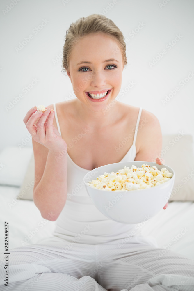 Natural cheerful blonde holding bowl of popcorn on bed Natural cheerful blonde holding bowl of popcorn on bed