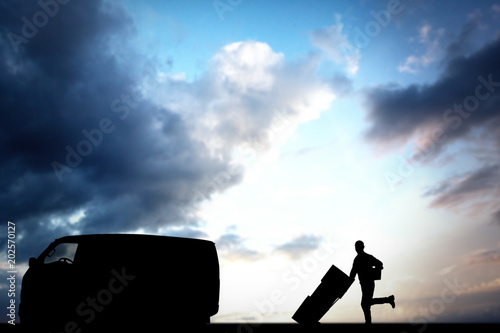 Happy delivery man with trolley of boxes running on white background against cloudy sky © vectorfusionart