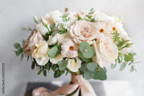 Fototapeta Naklejka Na Ścianę i Meble -  Wedding bouquet of white roses and buttercup on a wooden table. Lots of greenery, modern asymmetrical disheveled bridal bunch