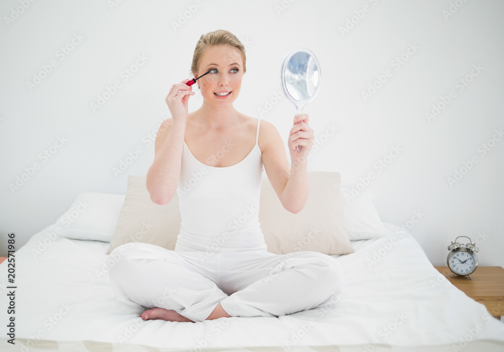 Natural happy blonde holding mirror and applying mascara Natural happy blonde holding mirror and applying mascara