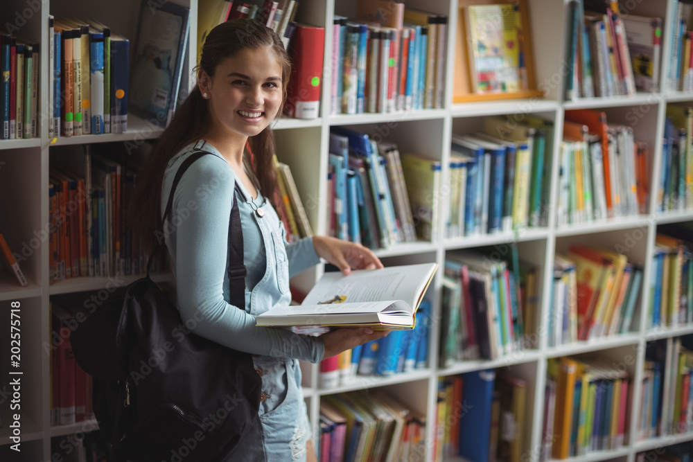 Portrait of happy schoolgirl holding book in library Portrait of happy schoolgirl holding book in library
