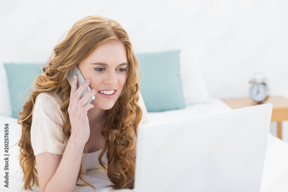 Smiling casual woman using laptop and cellphone in bed Smiling casual woman using laptop and cellphone in bed