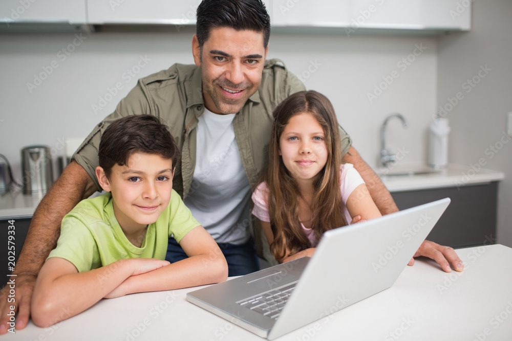 Smiling father with kids using laptop in kitchen Smiling father with kids using laptop in kitchen
