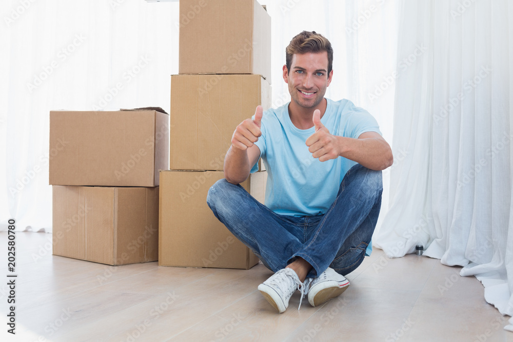 Man gesturing thumbs up with cardboard boxes in new house Man gesturing thumbs up with cardboard boxes in new house