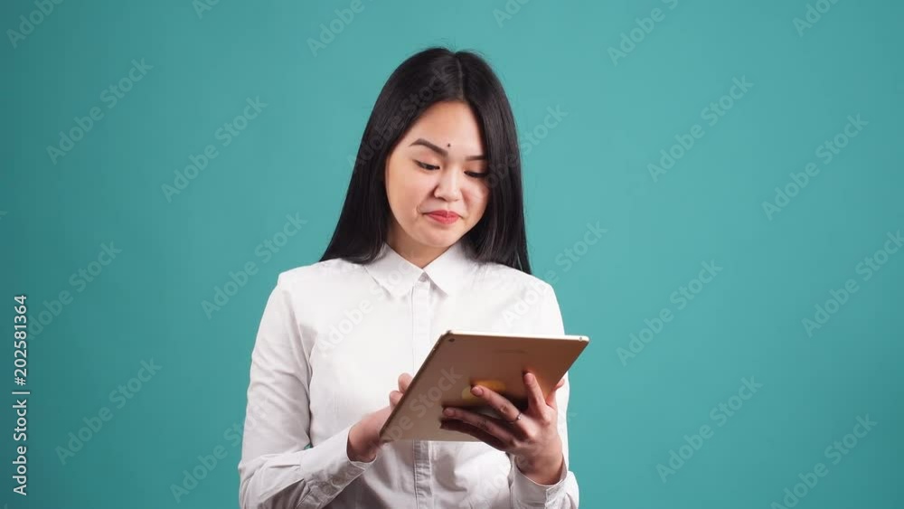 Happy Young Asian Girl Using Tablet Computer Isolated on a Blue Background. Happy Young Asian Girl Using Tablet Computer Isolated on a Blue Background.