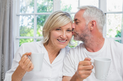 Mature man kissing woman while having coffee in bed