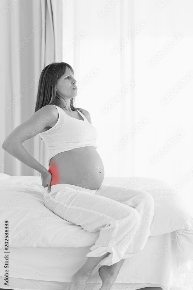 Good looking pregnant female having a back pain while sitting on a bed in her apartment
