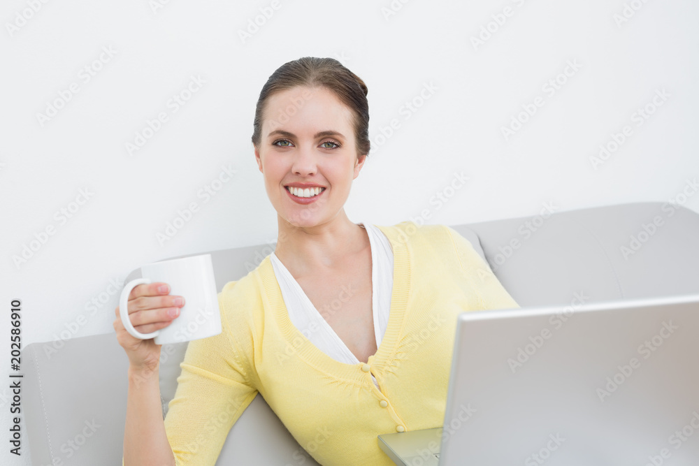 Smiling woman with coffee cup and laptop sitting at home Smiling woman with coffee cup and laptop sitting at home