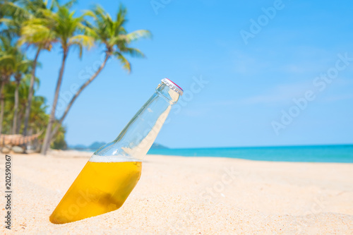Beer bottle on a sandy beach with palm tree. vintage color tone effect