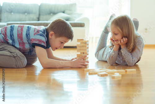 Two happy siblings playing a game with wooden blocks at home photo