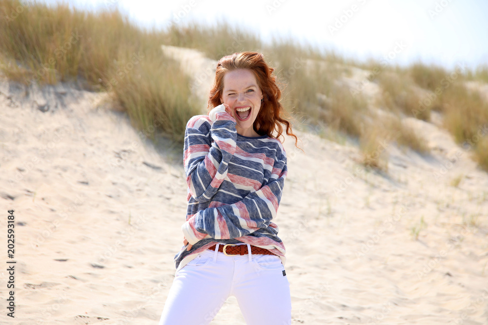 Hübsche rothaarige Frau am Strand lacht und zwinkert mit einem Auge Hübsche rothaarige Frau am Strand lacht und zwinkert mit einem Auge