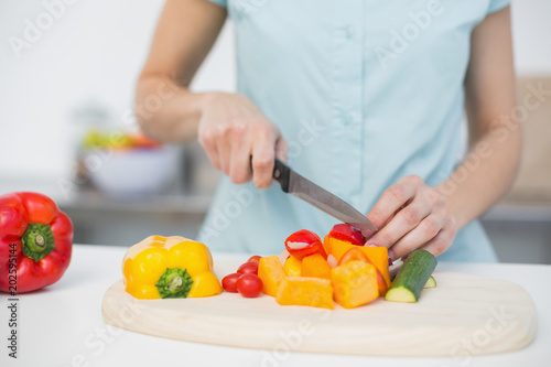 Mid section of young slender woman cutting vegetables