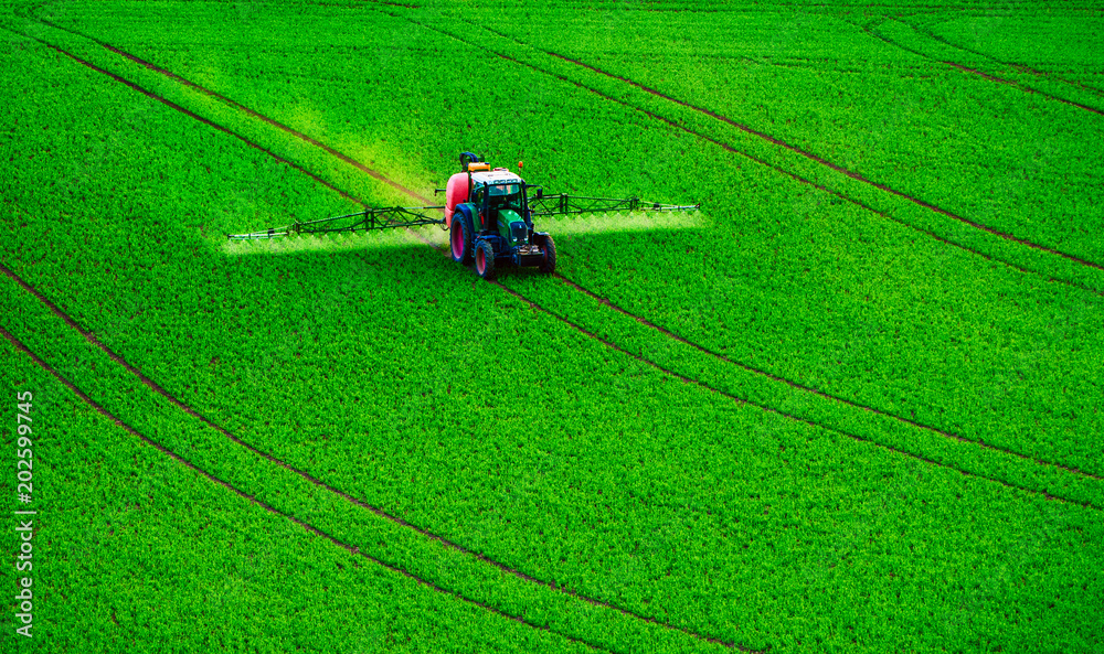 Farm machinery spraying insecticide to the green field, agricultural natural seasonal spring background
