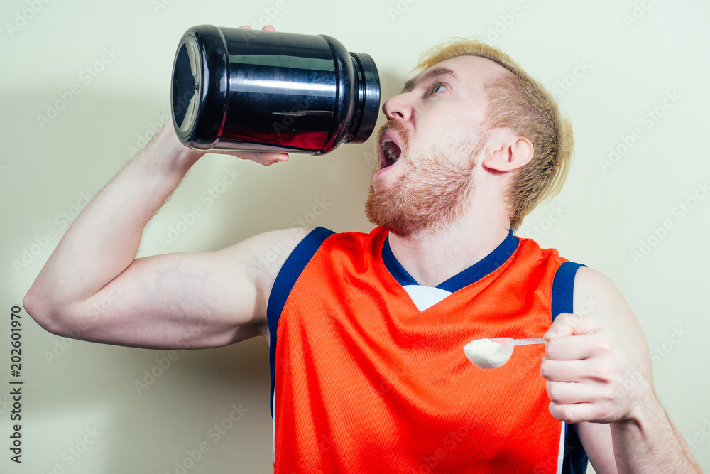 A blond man with a beard is holding a jar of protein in his hands. sports competition. doping. use of doping drugs A blond man with a beard is holding a jar of protein in his hands. sports competition. doping. use of doping drugs